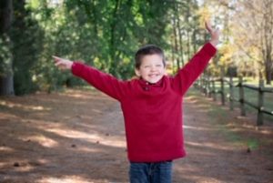 Boy with Smith-Kingsmore syndrome smiling, hands raised
