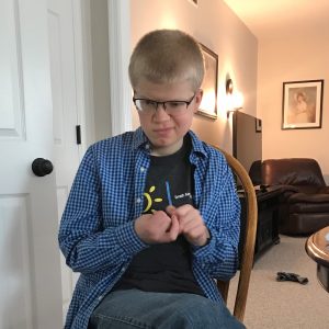 Teen with Smith-Kingsmore syndrome smiling while sitting and tapping hands