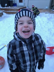 Boy with Smith-Kingsmore syndrome laughing wearing hat in the snow