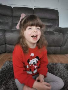 Girl with Smith-Kingsmore syndrome smiling sitting cross legged